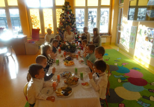 Pani dyrektor Maria Królikowska, pani Agnieszka Piekarska, pani Arleta Kalinowska oraz dzieci jedzą słodki i owocowy poczęstunek.